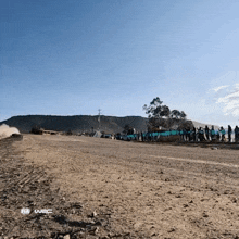 a group of people standing on the side of a dirt road watching a race