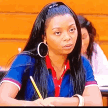a woman wearing hoop earrings and a blue shirt is sitting at a table with a pencil in her hand .