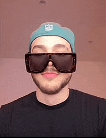 a man wearing a hat and sunglasses is looking at the camera .