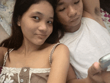 a man and a woman are laying on a bed and the woman is holding a cell phone