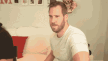 a man with a beard is sitting on a couch in a living room .