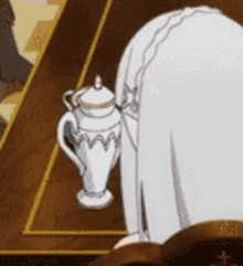a woman in a white dress is kneeling down next to a teapot on a table .