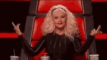 a woman is sitting in a red chair with her arms outstretched giving the middle finger .