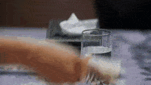 a person is holding a glass of water on a table with a tissue box in the background .