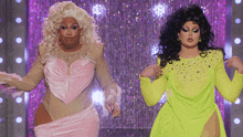 two drag queens are dancing on a stage in front of a purple curtain