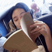a woman is reading a book on a plane while wearing a ring