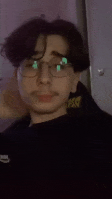 a man wearing glasses and a black sweater is covering his face with his hand .