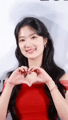 a young woman in a red dress is making a heart shape with her hands