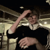 a young man wearing glasses and a black jacket is making a funny face and says dimples .