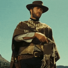 a man wearing a hat and a poncho is holding a gun in his hand
