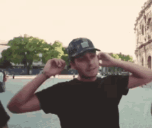 a man wearing a black shirt and a hat adjusts his ear buds