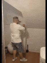 a man in a white shirt and blue shorts is standing in a bathroom next to a toilet
