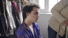 a man in a purple shirt is sitting in front of a clothes rack