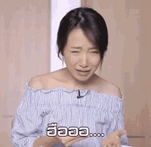 a woman in a blue and white striped off the shoulder top is making a funny face while holding something in her hand