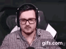 a man wearing headphones and glasses is sitting in a chair and talking into a microphone .