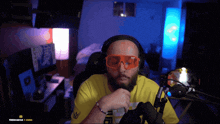 a man wearing a yellow shirt and orange sunglasses is sitting in front of a microphone with a watermark that says thescar34