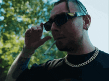 a man wearing sunglasses is smoking a cigarette and has a tattoo on his arm