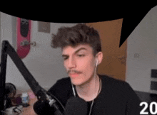 a young man with a mustache is sitting in front of a microphone .