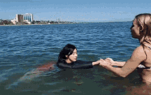 a woman in a bikini holds the hand of a mermaid in the water