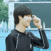 a young man wearing a black shirt is smiling and touching his face