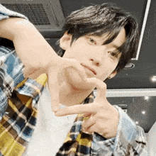 a young man wearing a plaid shirt is making a heart shape with his hands .