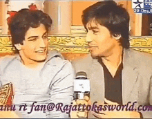 two men are sitting next to each other on a couch and talking to each other .