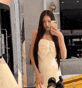 a woman in a white dress is taking a selfie in front of a mirror with her phone .
