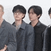 a group of young men are standing next to each other . one of the men is wearing glasses and a hat .