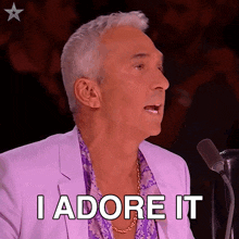 a man in a purple suit says " i adore it " in front of a microphone
