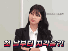 a woman in a suit and glasses is standing in front of a conference room