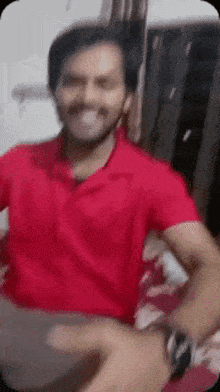 a man in a red shirt is smiling while sitting on a couch .