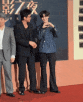 a man making a heart shape with his hands on a red carpet in front of a sign with chinese characters