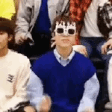 a group of young men are sitting in a row wearing sunglasses and a crown .