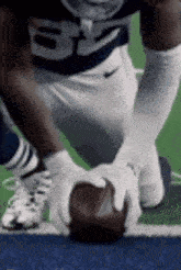 a football player is kneeling down on the field and holding a football in his hands .