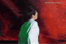 a man in a green shirt is standing in front of a red wall .