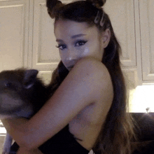 ariana grande is holding a cat in her arms in a kitchen .