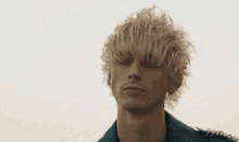 a man with blonde hair and a tattoo on his neck is wearing a blue leather jacket .