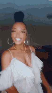 a woman in a white dress and hoop earrings is standing in front of a mirror .