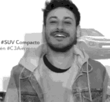 a man with a beard is smiling in front of a car .