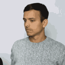 a man wearing a grey striped sweater looks to his left
