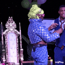 a man in a suit stands next to a woman in a blue outfit with the word muffin on the back of her pants