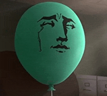 a green balloon with a face drawn on it is sitting on a table .