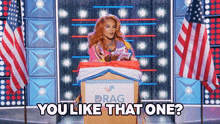 a drag queen is giving a speech at a podium with the words `` you like that one '' written below her .