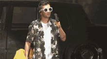 a man wearing sunglasses and a floral shirt singing into a microphone