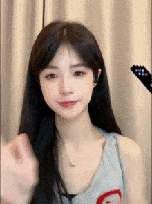 a girl with long black hair is wearing a necklace and a tank top with a g on it .