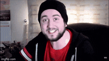 a man with a beard wearing a black hat and a red shirt