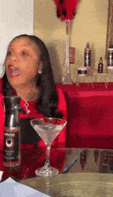 a woman is sitting at a table with a martini glass and a spray bottle that says ' beard ' on it