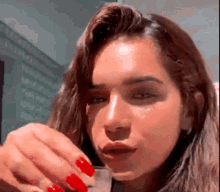 a woman with long red nails is drinking from a small glass .
