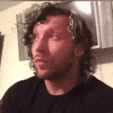 a man with curly hair and a beard is wearing a black shirt and looking at the camera .