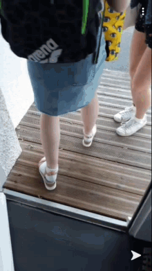 a woman wearing a blue skirt and white sandals is standing on a wooden floor